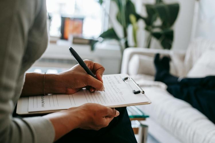 Female counsellor writing session notes client on couch